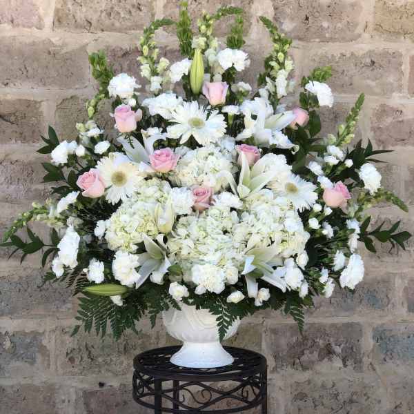 White floral arrangement with pink roses in a white urn vase