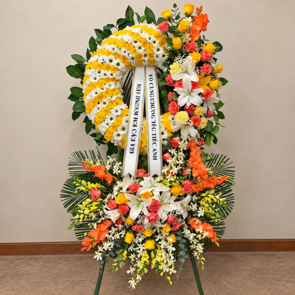 Large standing floral wreath with white and yellow flowers and a ribbon