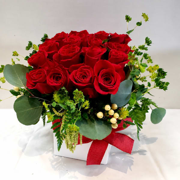 Red roses arranged in a white box with greenery and a red ribbon