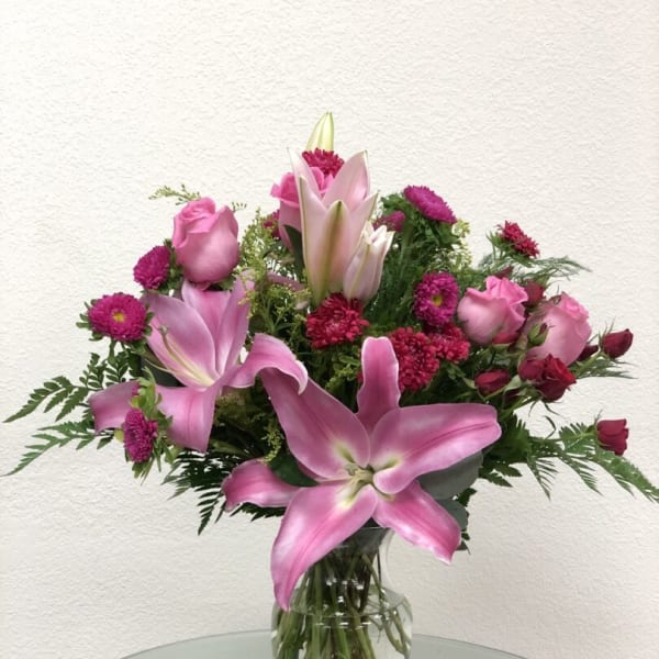 Pink lilies and roses arranged in a clear glass vase