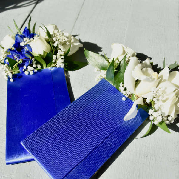 Two blue ribbon corsages with white flowers on a light surface