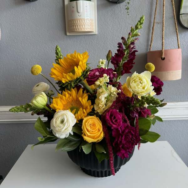 Mixed bouquet with sunflowers, roses, and snapdragons in a black vase