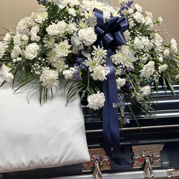White floral casket spray with a navy ribbon on a black casket