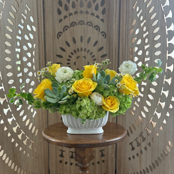 Yellow and white roses arranged in a white vase with succulents