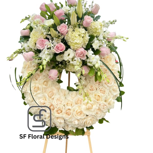 Large ivory rose wreath with pink roses, lilies, and white blooms arranged on top, displayed on a wooden easel.
