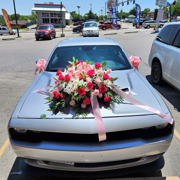 Large pink and white floral arrangement with ribbons on a silver car hood