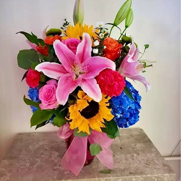 Colorful bouquet with pink lilies, roses, sunflowers, and blue hydrangeas in a vase
