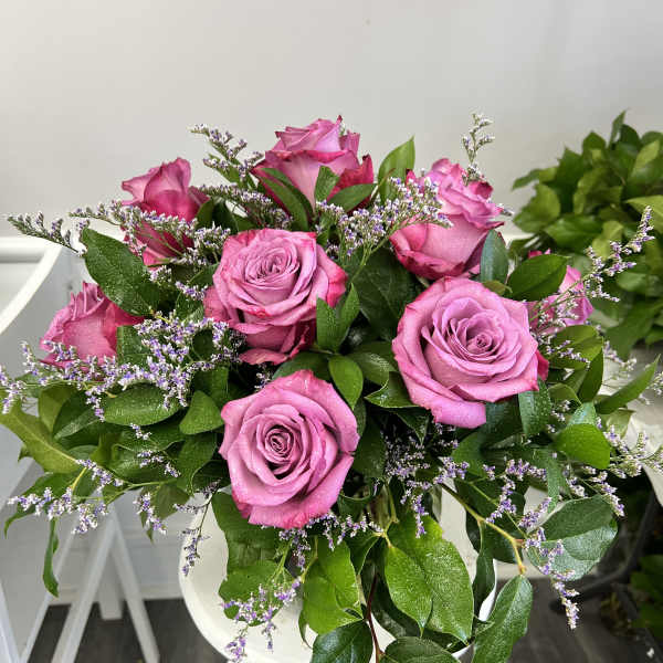 Hand-tied bouquet of bright pink roses with small purple filler flowers in a rounded design