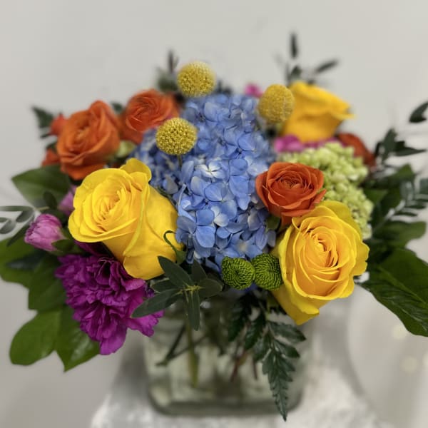 Colorful bouquet with roses, hydrangea, and purple blooms in a glass vase