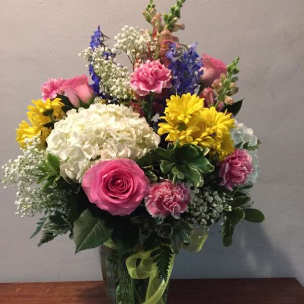 Mixed bouquet in a glass vase with pink roses, white hydrangea, and yellow daisies