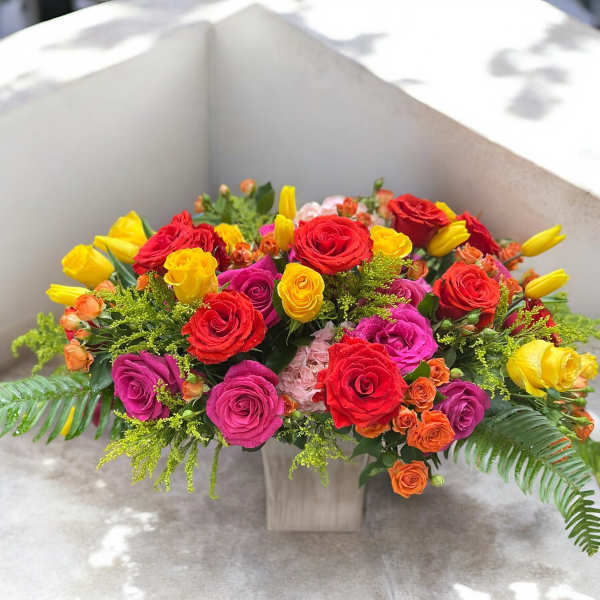 Bright mixed bouquet of roses and tulips in a square vase