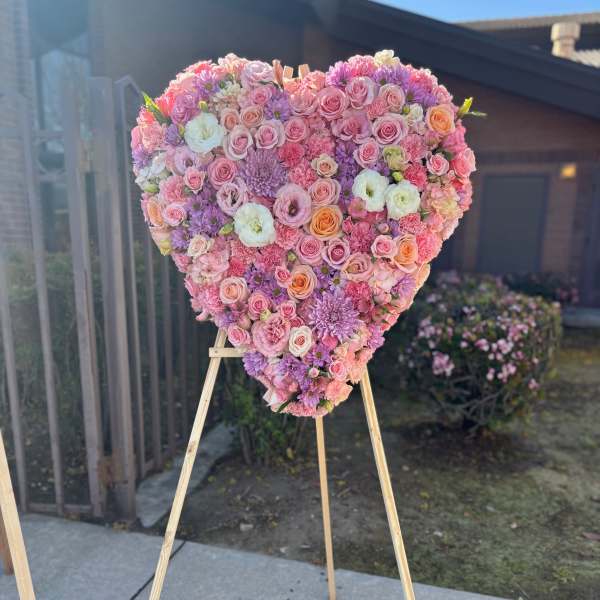 Heart-shaped floral arrangement on a wooden easel with pink and purple blooms