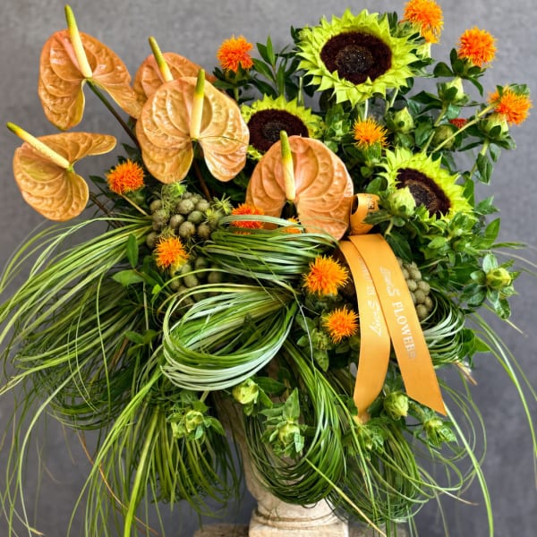 Tropical arrangement with orange anthuriums, sunflowers, and orange ribbon in a vase