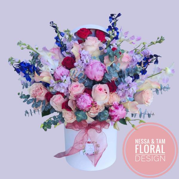 Bouquet of pink and red roses with blue flowers in a white hatbox