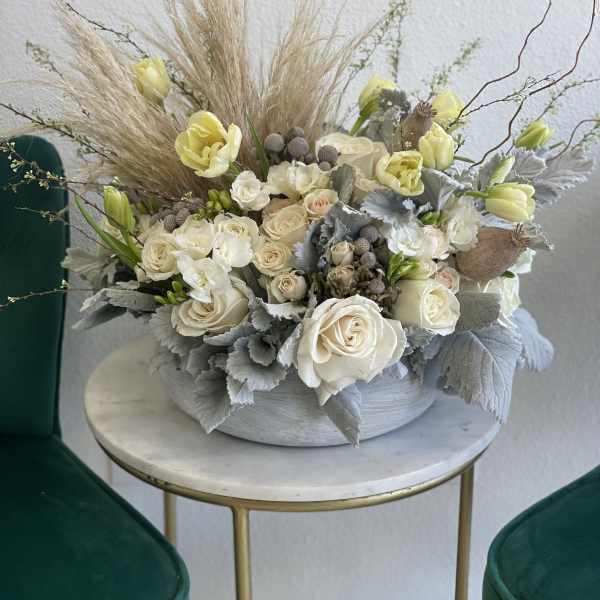 Cream roses and pale yellow tulips in a low gray bowl with dried grasses
