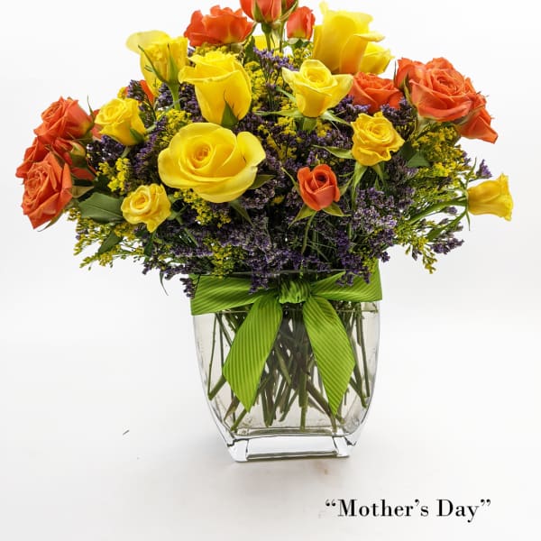 Yellow and orange roses in a clear glass vase with a green ribbon
