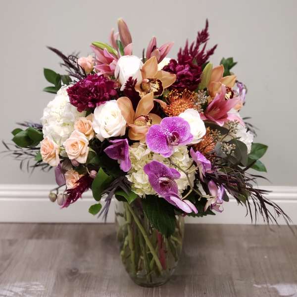 Mixed bouquet of orchids, roses, and hydrangeas in a glass vase