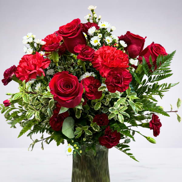 Red roses and carnations in a glass vase with small white daisies