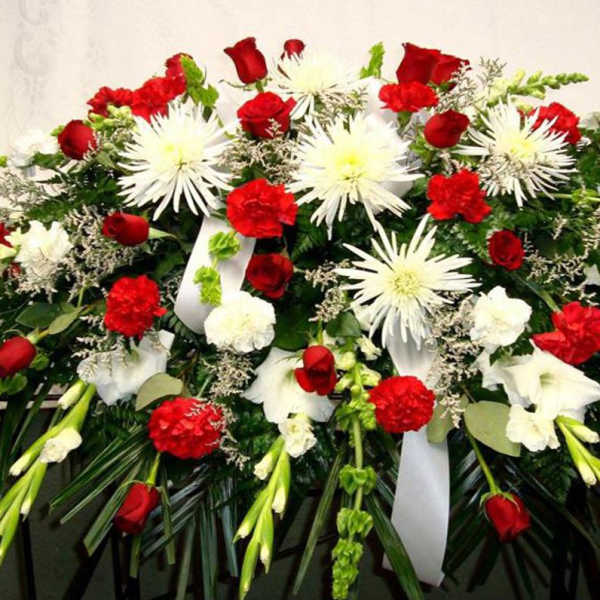 Red roses, carnations, and white spider mums in a large sympathy casket spray with white ribbons