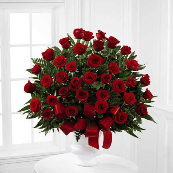 Large arrangement of red roses in a white urn with red ribbon bow.