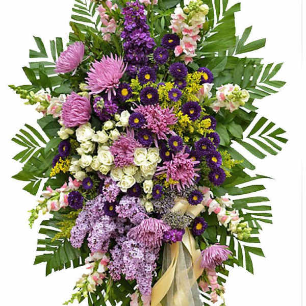 Tall standing spray of purple, pink, and white flowers with large green leaves on an easel