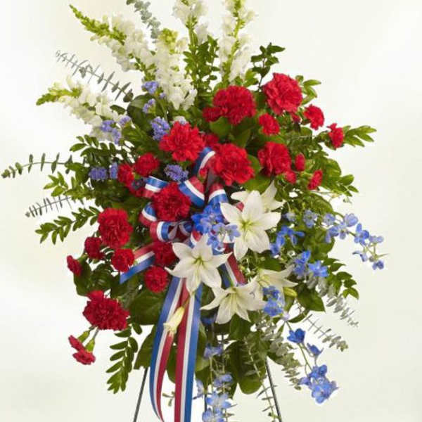 Tall red, white, and blue standing spray of flowers on a metal easel with a patriotic ribbon.