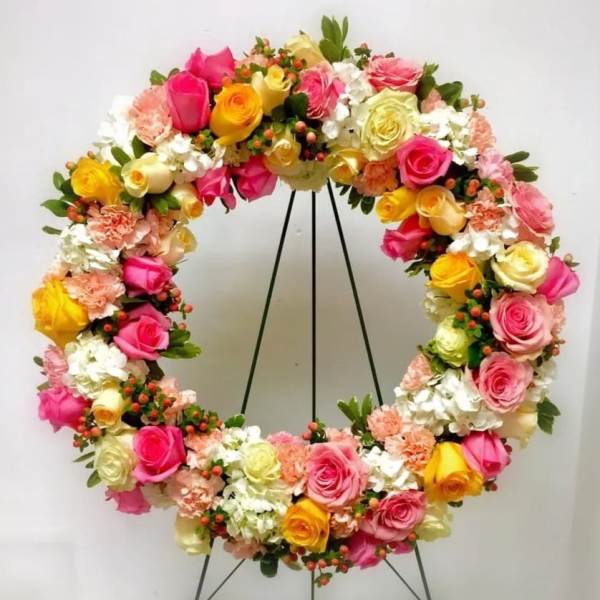 Circular floral wreath with pink, yellow, and white roses on a stand