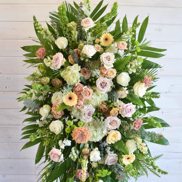 Large standing spray of pastel roses and mixed flowers with tropical greenery