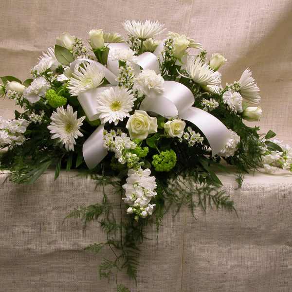 White floral casket spray with ribbon on a beige cloth backdrop