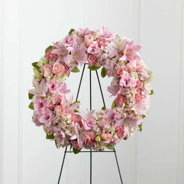 Pink floral wreath with lilies, roses, and carnations on a metal easel