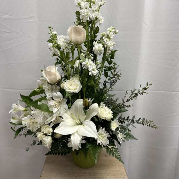Tall white floral arrangement with lilies and roses in a green vase