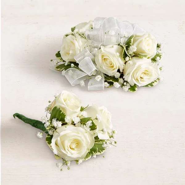 Two white rose boutonnieres with ribbon accents on a light background