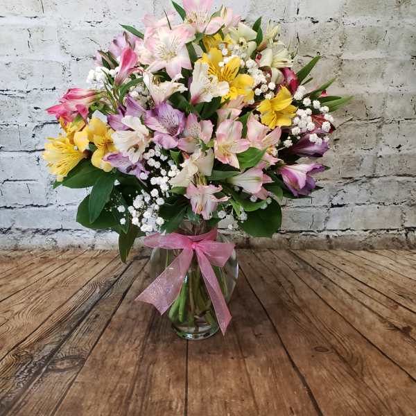 Mixed pink, yellow, and white flowers in a glass vase with a pink ribbon