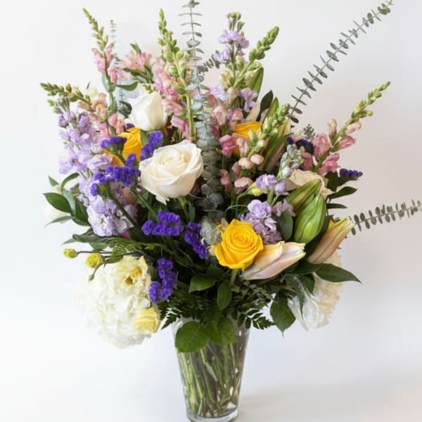 Mixed bouquet of roses, lilies, and purple flowers in a clear glass vase