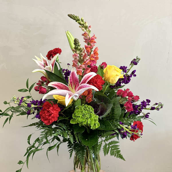 Mixed bouquet with lilies, roses, carnations, and snapdragons in a glass vase