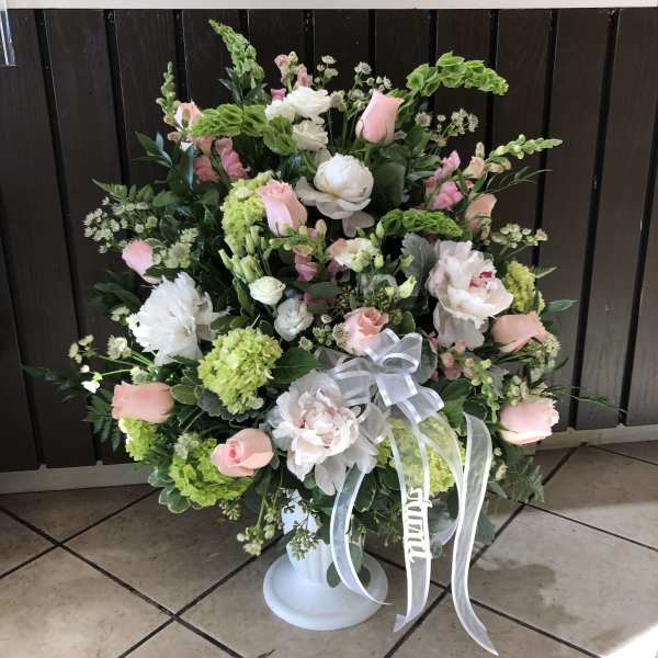 Large pink and white floral arrangement in a white pedestal vase with ribbon