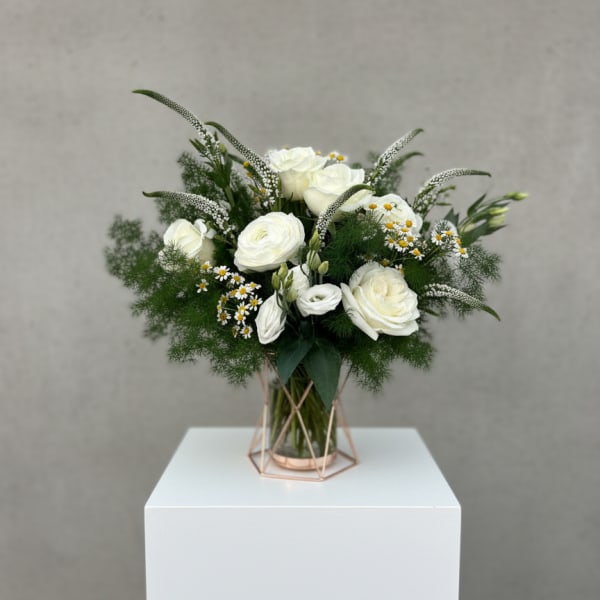 White roses and small daisies in a glass vase with greenery