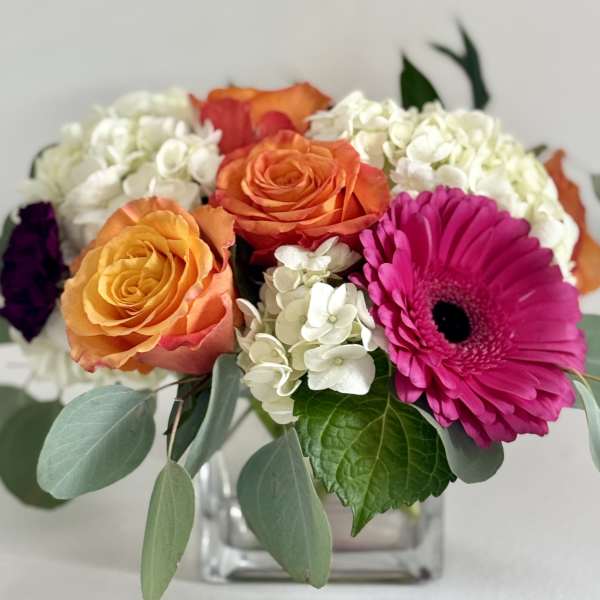 Bouquet of orange roses, white hydrangeas, and a pink gerbera daisy in a glass vase