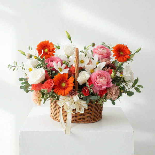 Basket arrangement of pink, white, and orange flowers with a ribbon bow