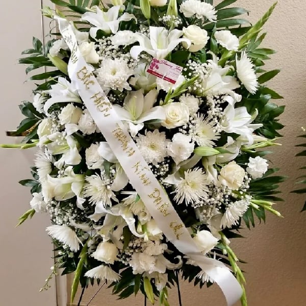 Large white funeral wreath with lilies, roses, and chrysanthemums on an easel