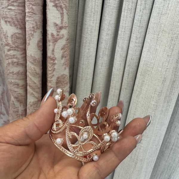 Hand holding a small rose-gold jeweled crown