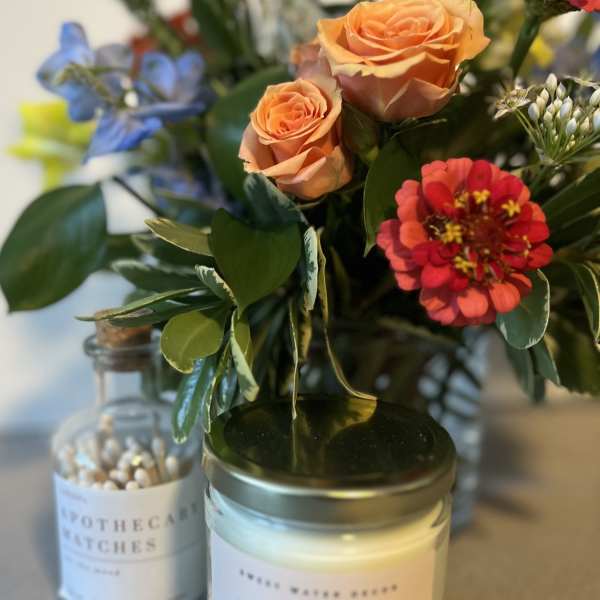 Small floral arrangement in a glass jar with roses and a red zinnia, beside candles