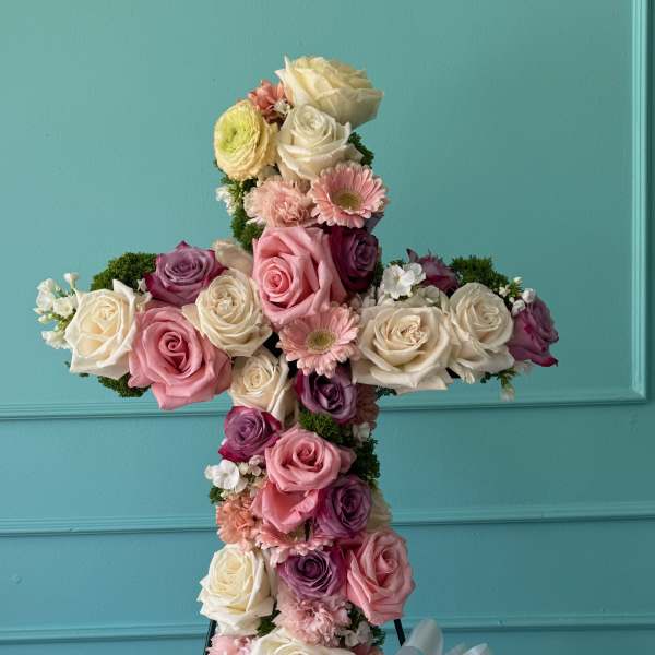 Cross-shaped floral arrangement of roses and pink blooms on a stand