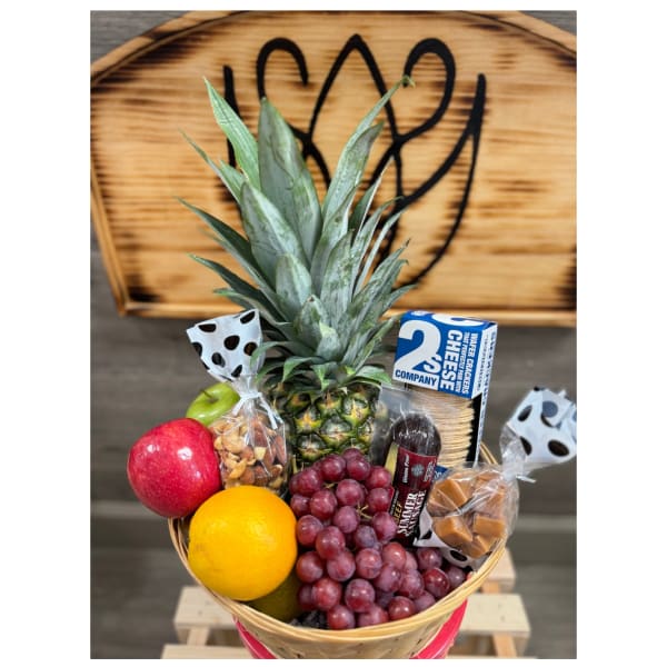 Gift basket with pineapple, grapes, apples, citrus, nuts, cheese, sausage, and caramels in a woven container