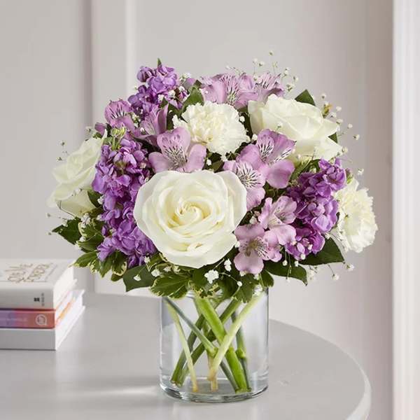 Bouquet of white roses and purple flowers in a clear glass vase