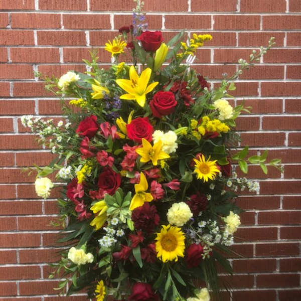 Standing floral spray with red roses, yellow lilies, and sunflowers