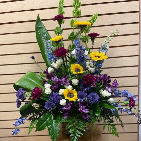 Tall mixed flower arrangement in a bronze vase with yellow, purple, blue, and white blooms