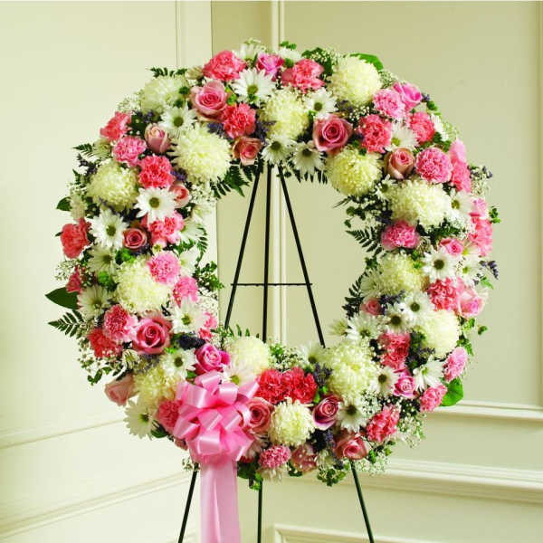 Pink and white floral wreath on a black stand with a pink ribbon
