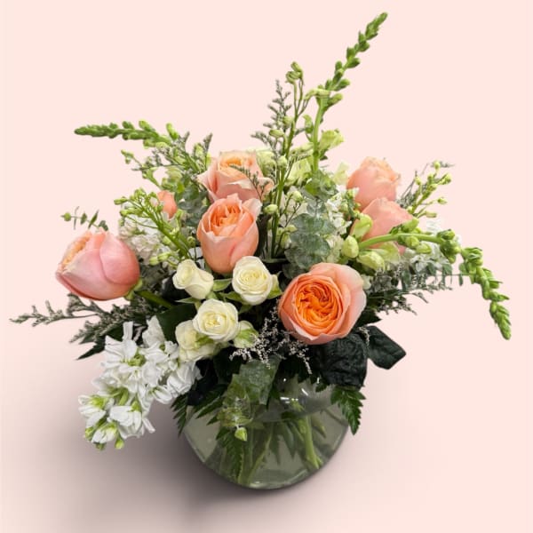 Peach and white roses arranged in a glass vase