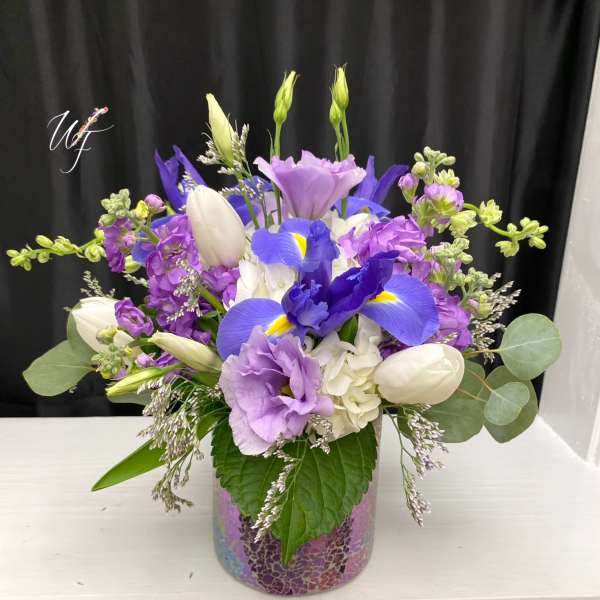 Purple and white floral arrangement in a mosaic glass vase